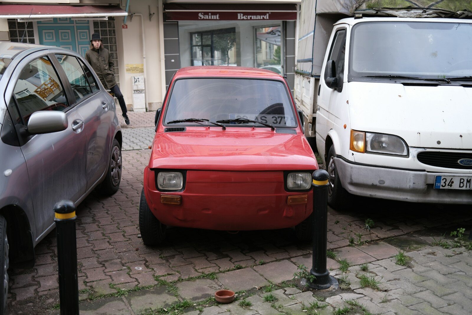 A small red car parked between two vehicles.
